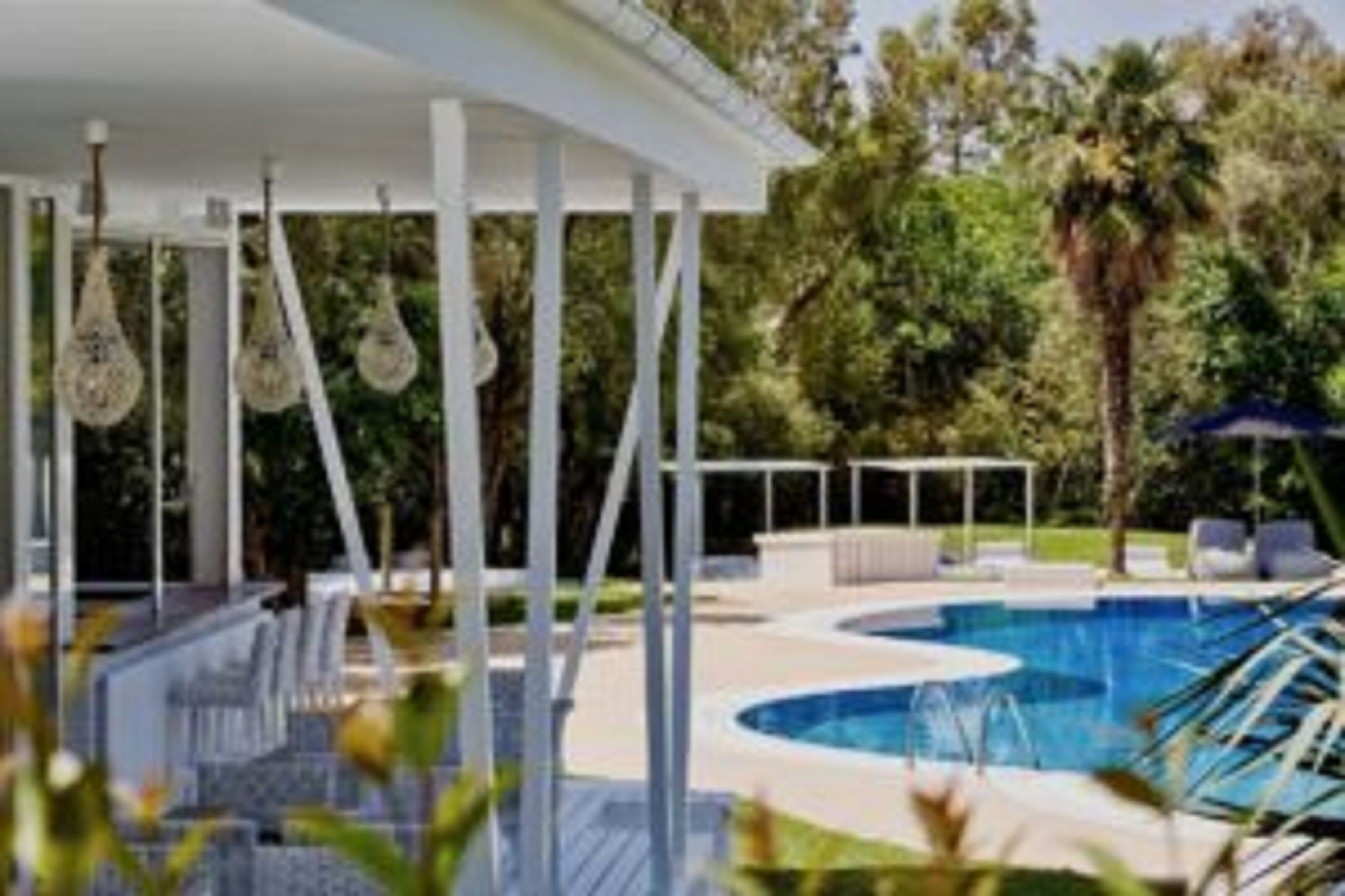 A pool area with a covered seating area, lounge chairs, and a palm tree in the background.