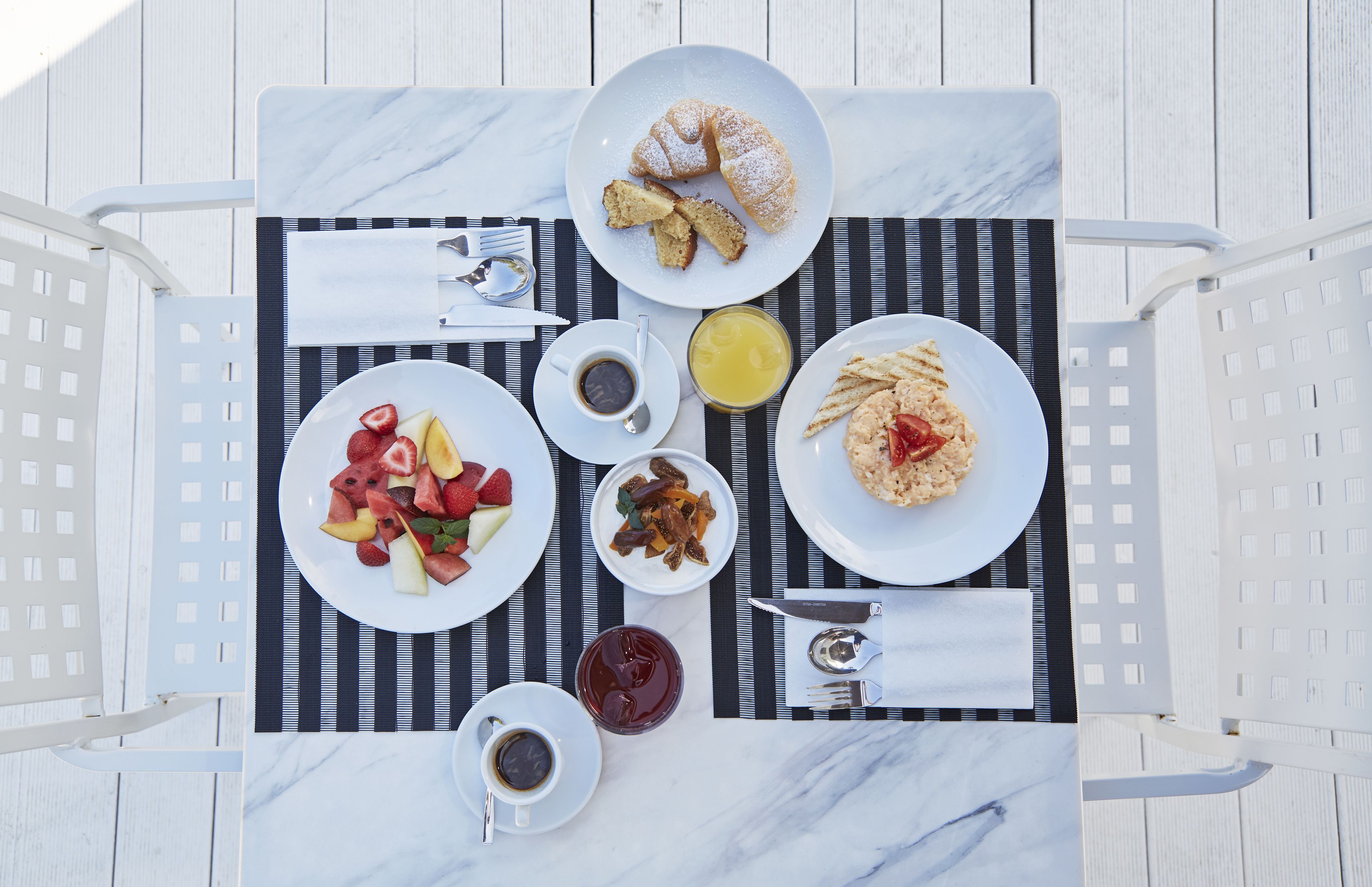 Una mesa de desayuno con platos de comida, tazas de café y un vaso de zumo de naranja.