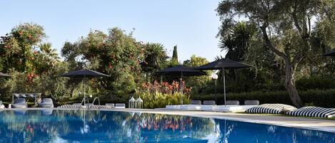 A swimming pool with lounge chairs and umbrellas, surrounded by lush greenery and trees.