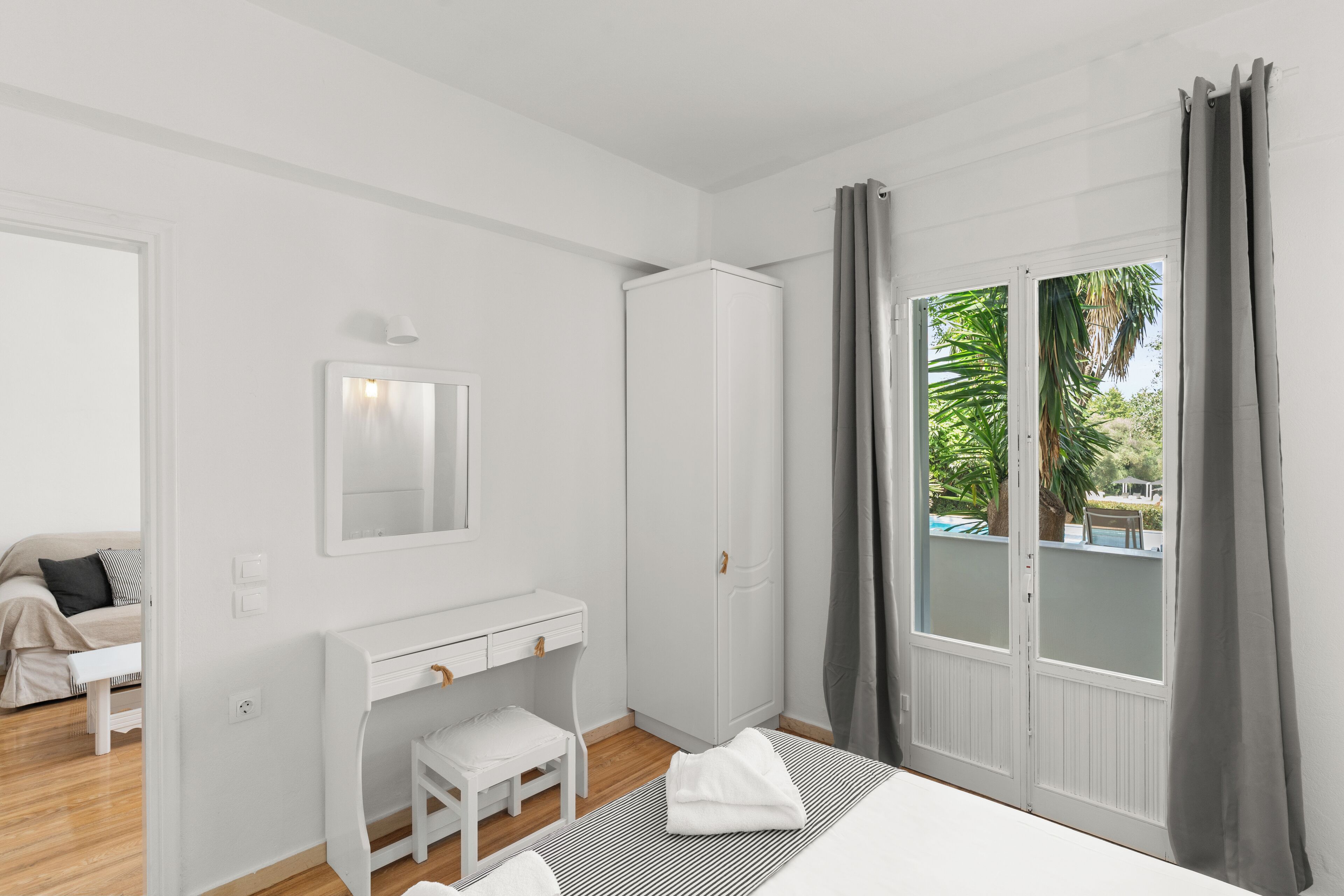 A bedroom with a bed, a vanity with a mirror, a wardrobe, and a view of a pool through a glass door.