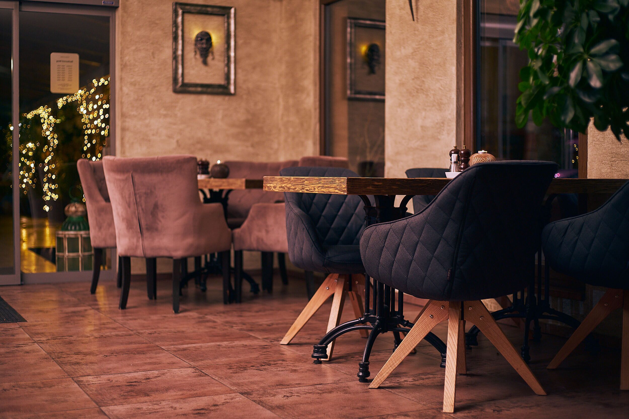 A cozy indoor seating area with cushioned chairs and a wooden table, featuring a rustic floor and framed artwork on the walls.