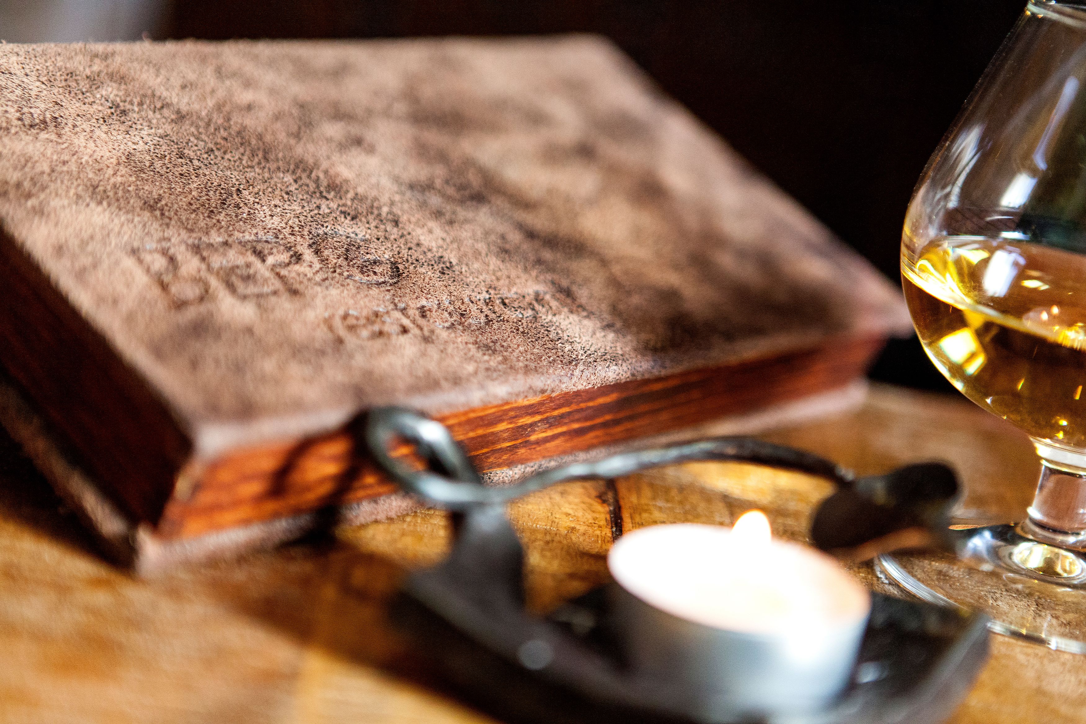Primer plano de una mesa de madera con un libro, una tetera y una copa de vino.