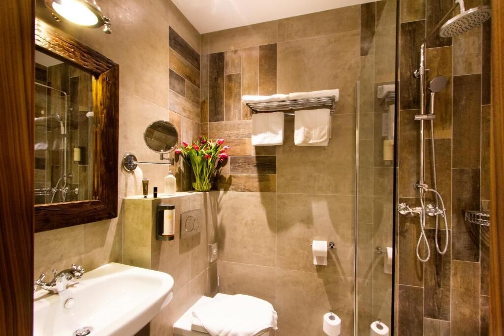 A modern bathroom with a bathtub, a shower, and a toilet. There is a mirror, a towel rack, and a small vase with flowers.