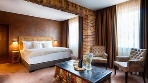 A hotel room with a large bed, two armchairs, a wooden coffee table, and a brick accent wall. - Penzión Berg (Bratislava)