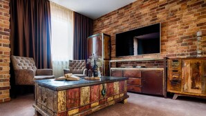 A living room with a brick wall, a large flat-screen TV, a tufted sofa, and a wooden coffee table. - Penzión Berg (Bratislava)