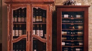 Two wooden wine cabinets with glass doors, each containing multiple bottles and wine boxes. - Penzión Berg (Bratislava)
