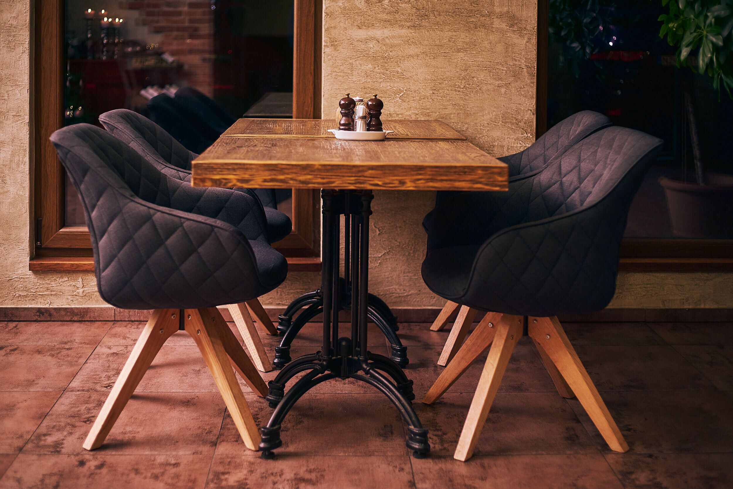 A wooden table with two upholstered chairs, a salt and pepper set, and a potted plant.