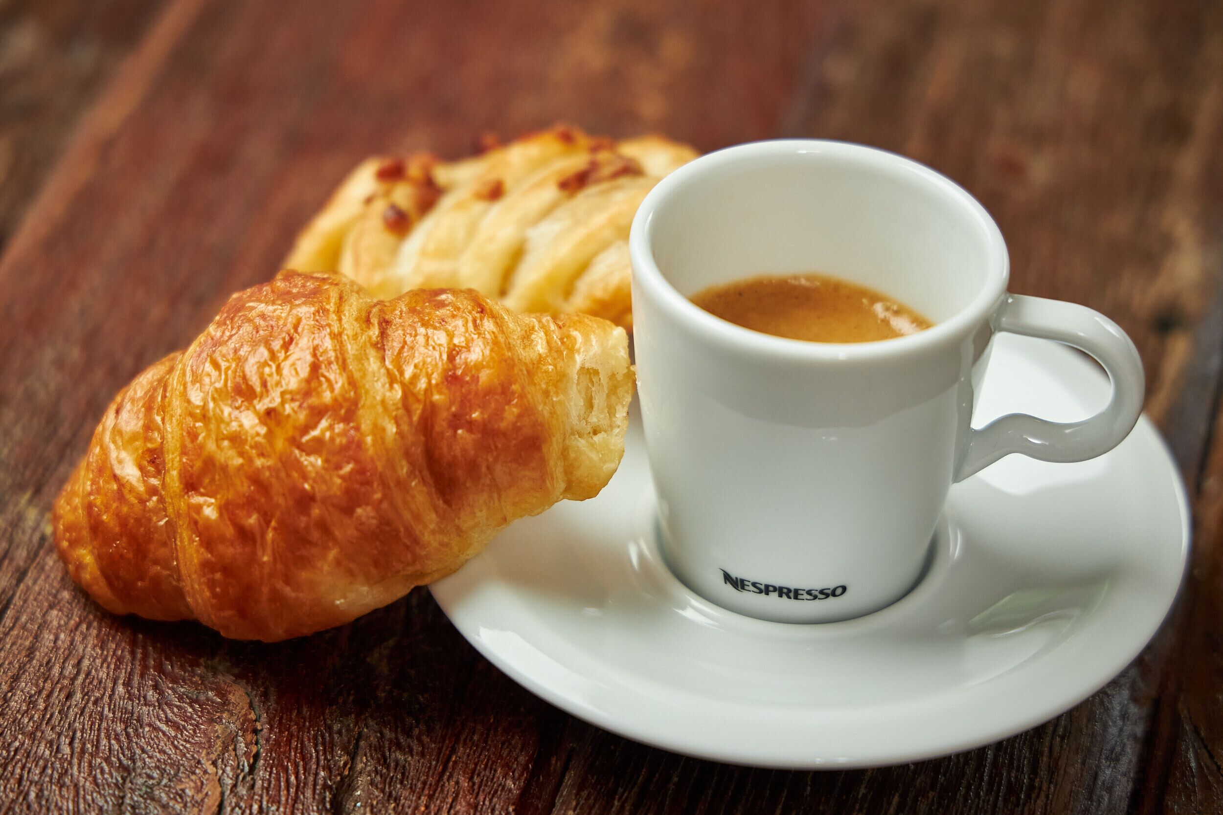 A croissant and a cup of coffee on a white saucer.