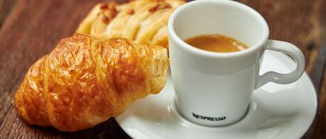 A croissant and a cup of coffee on a white saucer.