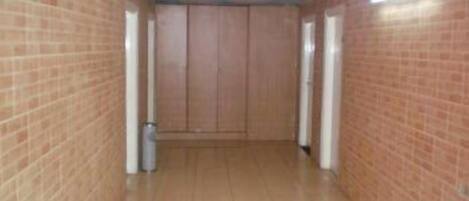A narrow hallway with brick walls and wooden flooring, leading to a door at the end.