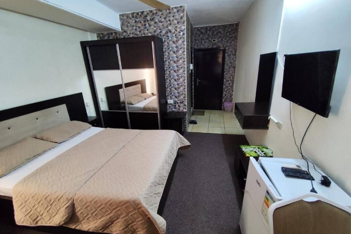 A hotel room with a bed, a desk with a computer, a TV, and a wardrobe.
