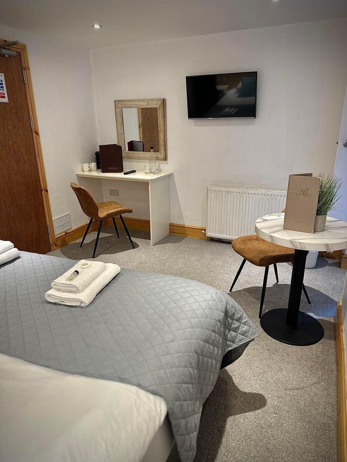 A hotel room with two beds, a desk with a chair, a small table with a plant, a TV on the wall, and a radiator.