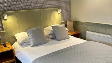 Una cama bien hecha con una colcha gris acolchada, un cabecero con luces empotradas en la pared, y un papel tapiz decorativo sobre la cama.