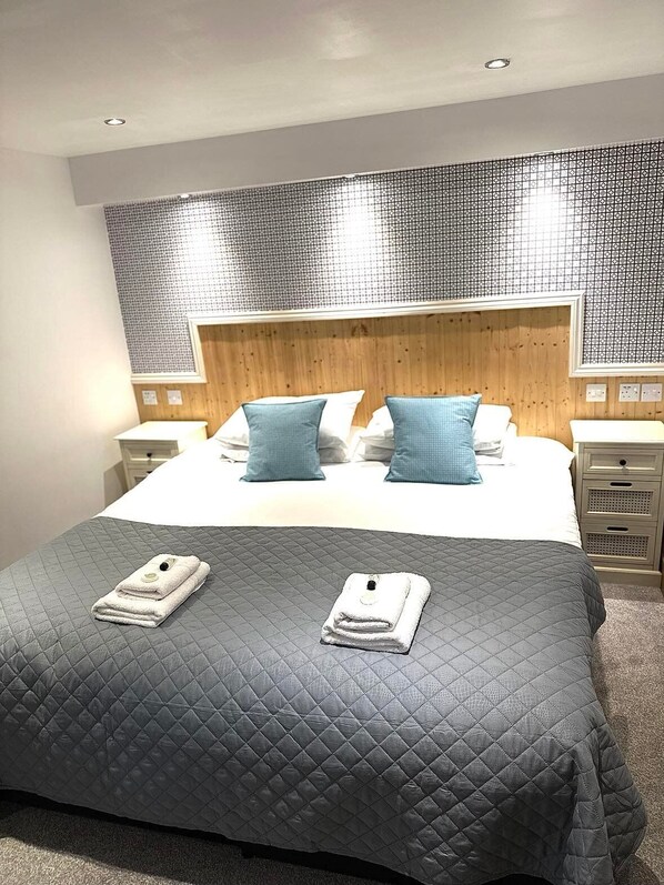 A hotel room with a large bed, two nightstands, a wooden headboard, and a patterned wall.