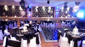 A banquet hall with round tables, white chairs, and black tablecloths. - Nithsdale Hotel (Sanquhar)
