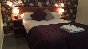 A neatly made bed with a purple bedspread and two pillows, flanked by two bedside lamps on wooden nightstands.