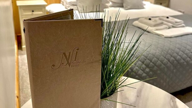 A hotel room with a bed, a nightstand, a bedside table with a book, and a plant. - Nithsdale Hotel (Sanquhar)
