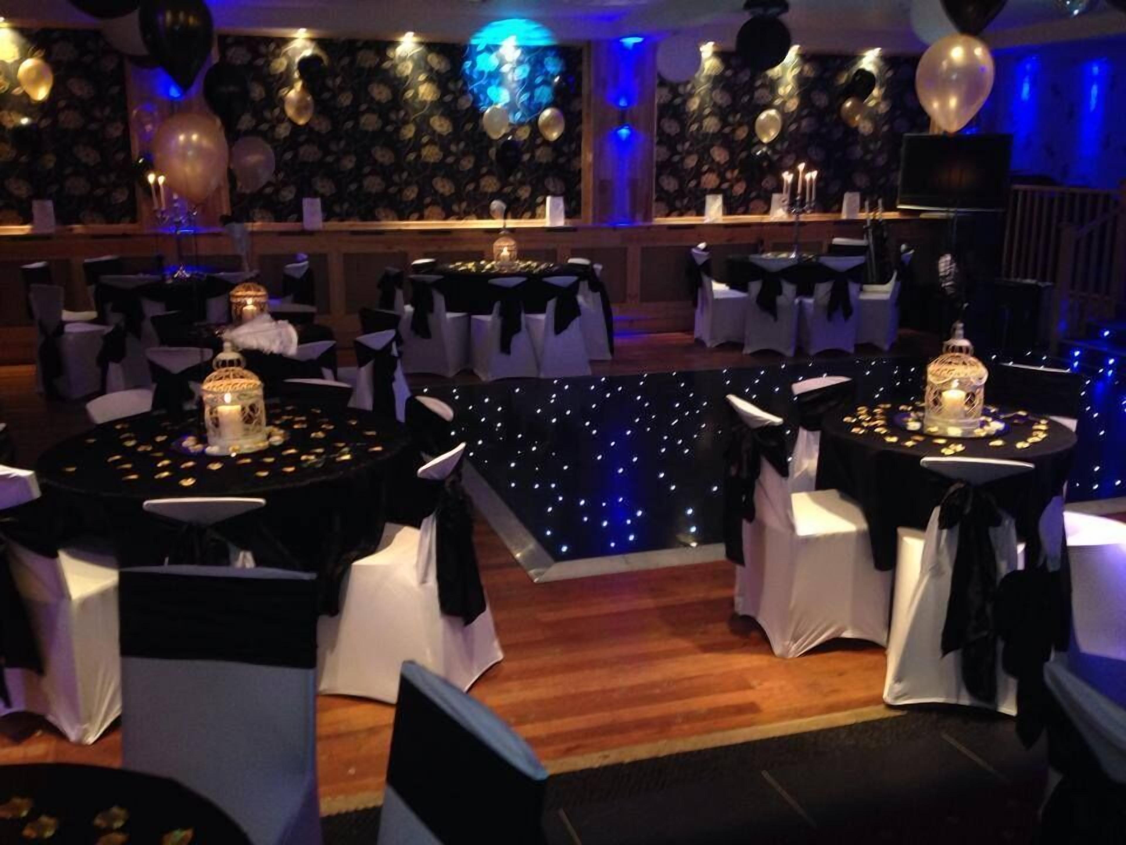 Une salle de banquet avec des tables rondes, des chaises blanches et des nappes noires.