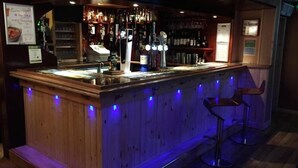 A bar area with a wooden counter, bar stools, and a variety of bottles and glasses. - Nithsdale Hotel (Sanquhar)