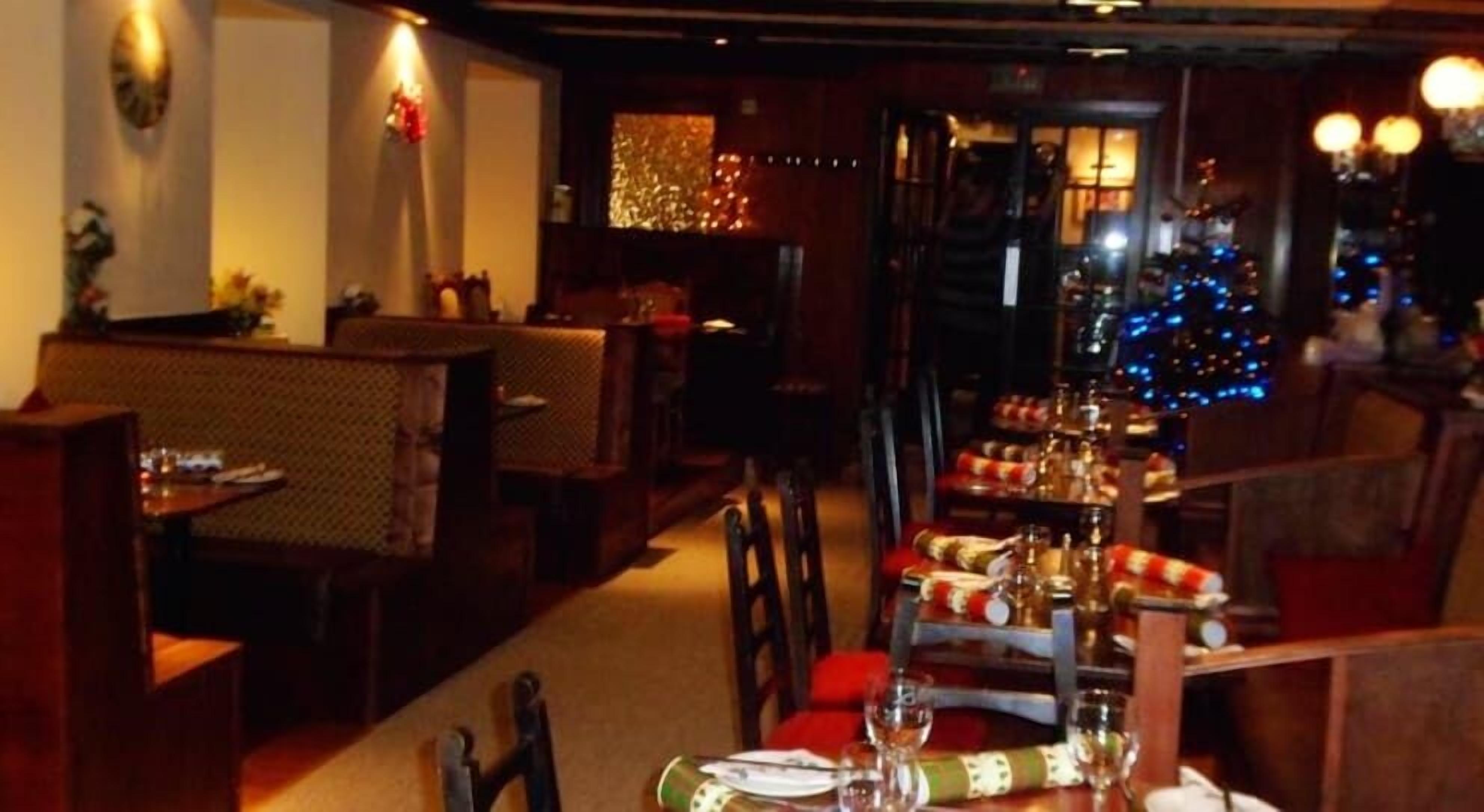 A restaurant with booths and tables set for dining, a Christmas tree in the background, and warm lighting.