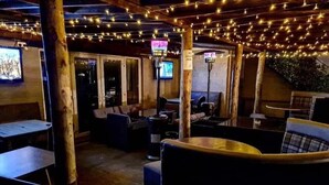 An outdoor seating area with tables and chairs, string lights overhead, and a TV screen visible in the background. - Nithsdale Hotel (Sanquhar)