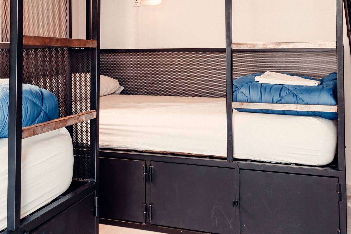 A bunk bed room with a wooden ceiling and metal frame, featuring multiple beds and storage cabinets.