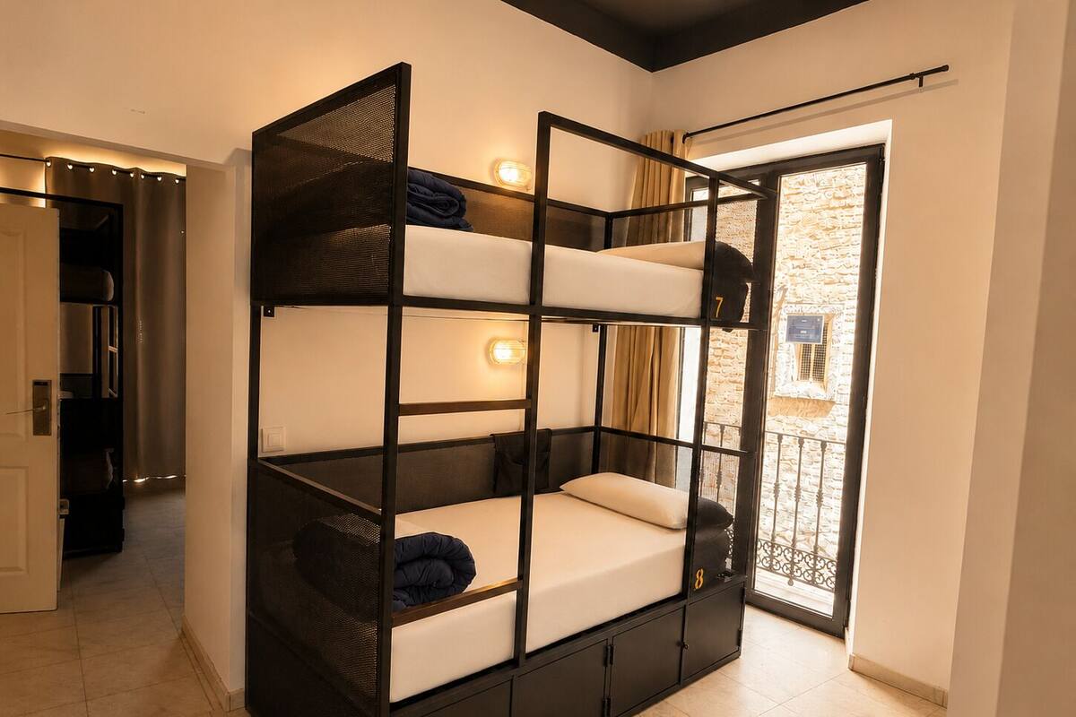 A bunk bed with a mesh headboard, a small window with curtains, and a door leading to another room.