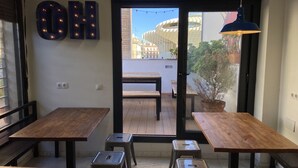 L’intérieur d’un café, avec des tables et des tabourets en bois, une grande enseigne lumineuse en forme de « OH », et une vue sur un bâtiment à travers la porte en verre.