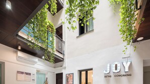 Un espace de coworking moderne, doté d’une table en bois, de chaises de bureau, d’un canapé gris et de plantes suspendues.