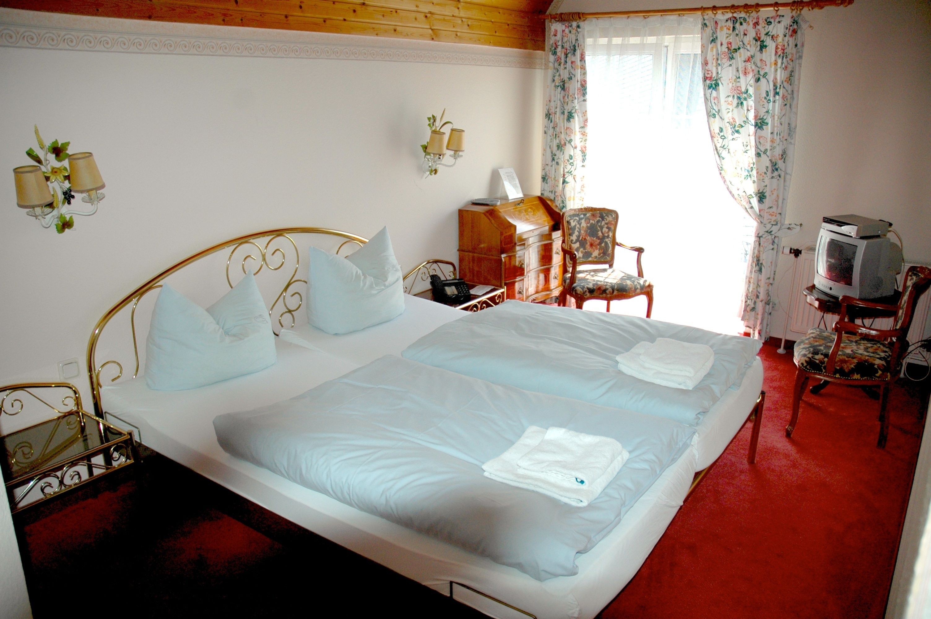 Ein Hotelzimmer mit einem großen Bett, einem Holzkapfen, einem Sessel, einem Fernseher und einem Schreibtisch mit Lampe.