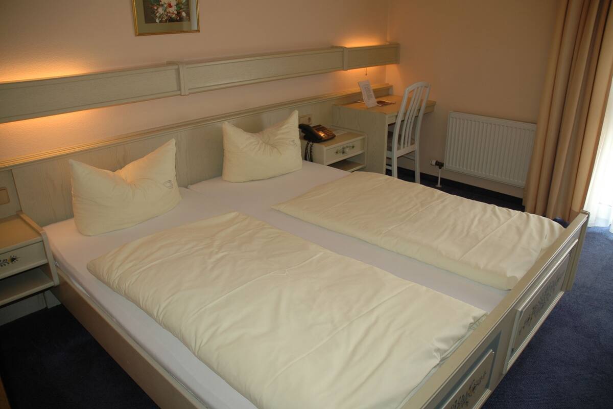Un lit double avec deux oreillers, une table de chevet avec un téléphone, une chaise et un bureau avec une lampe.