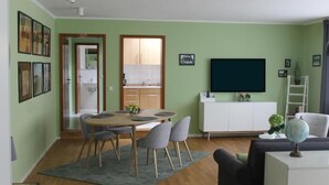 Een woonkamer met een eethoek, een televisie, en een keuken zichtbaar door een open deur.