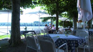 Een terras met tafels en stoelen, met uitzicht op een waterpartij.
