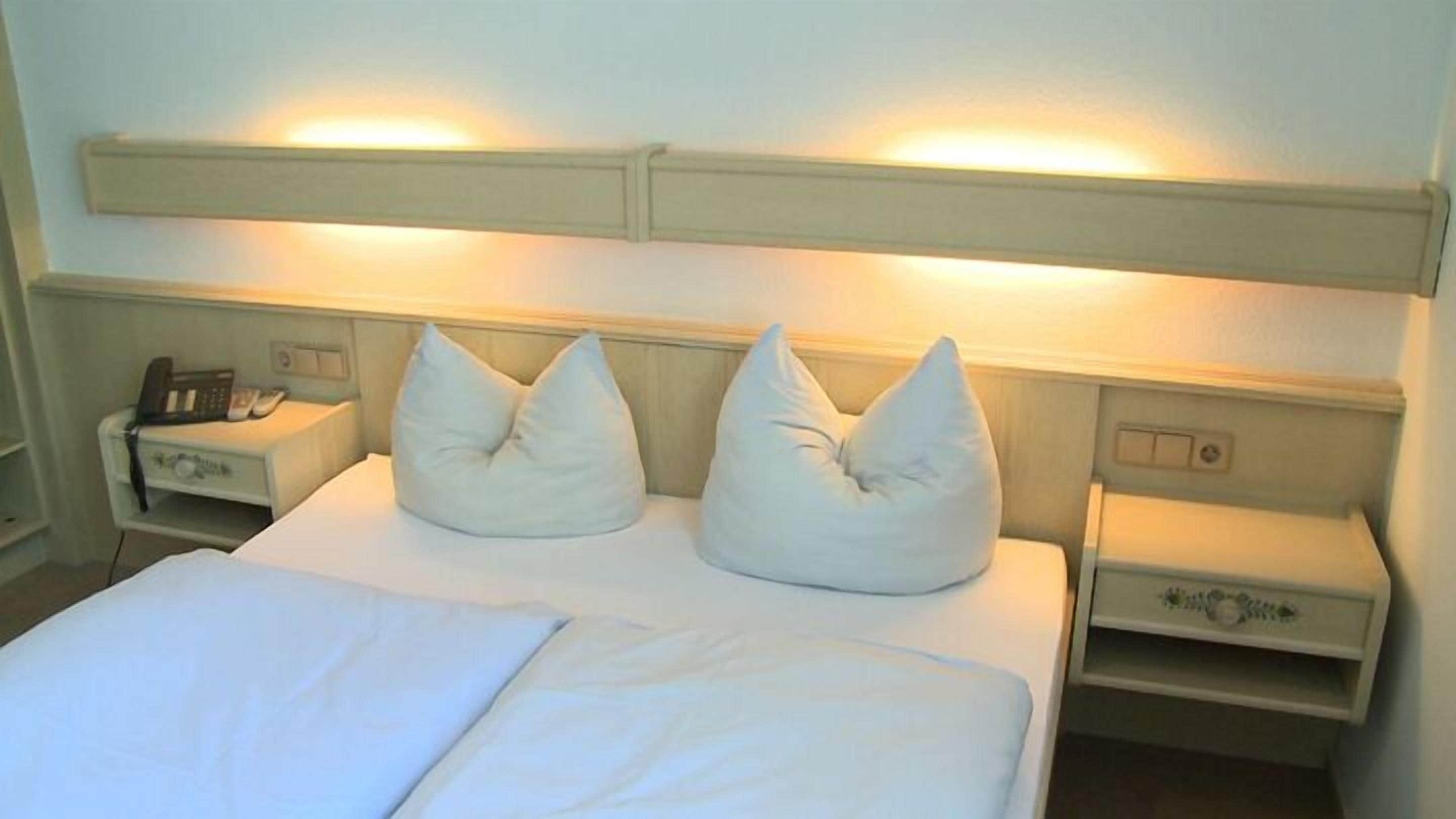 Een hotelkamer met een bed, twee nachtkastjes en een hoofdeinde met ingebouwde verlichting.