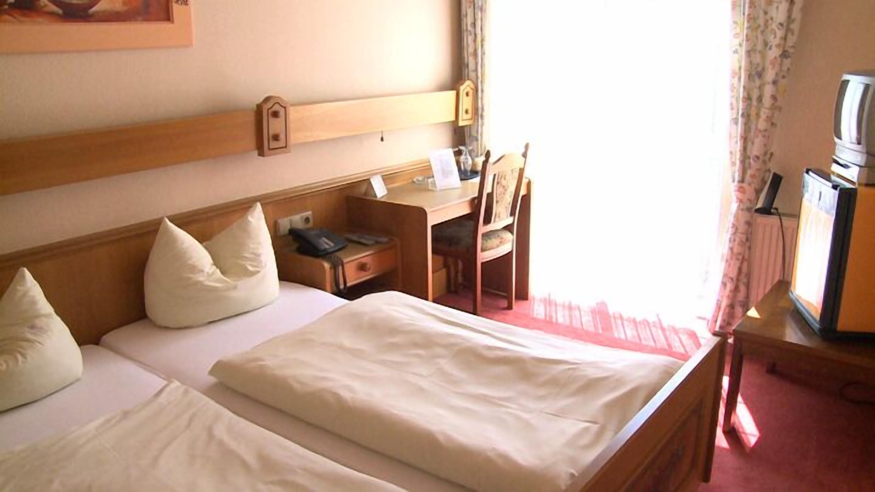 A hotel room with two beds, a desk, a chair, a television, and a window with curtains.