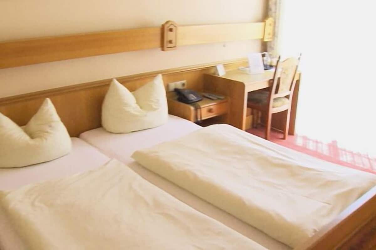 Une chambre d’hôtel avec deux lits, chacun doté de draps et d’oreillers blancs, d’une tête de lit en bois, d’un petit bureau avec une chaise et d’une fenêtre donnant sur un paysage agréable.