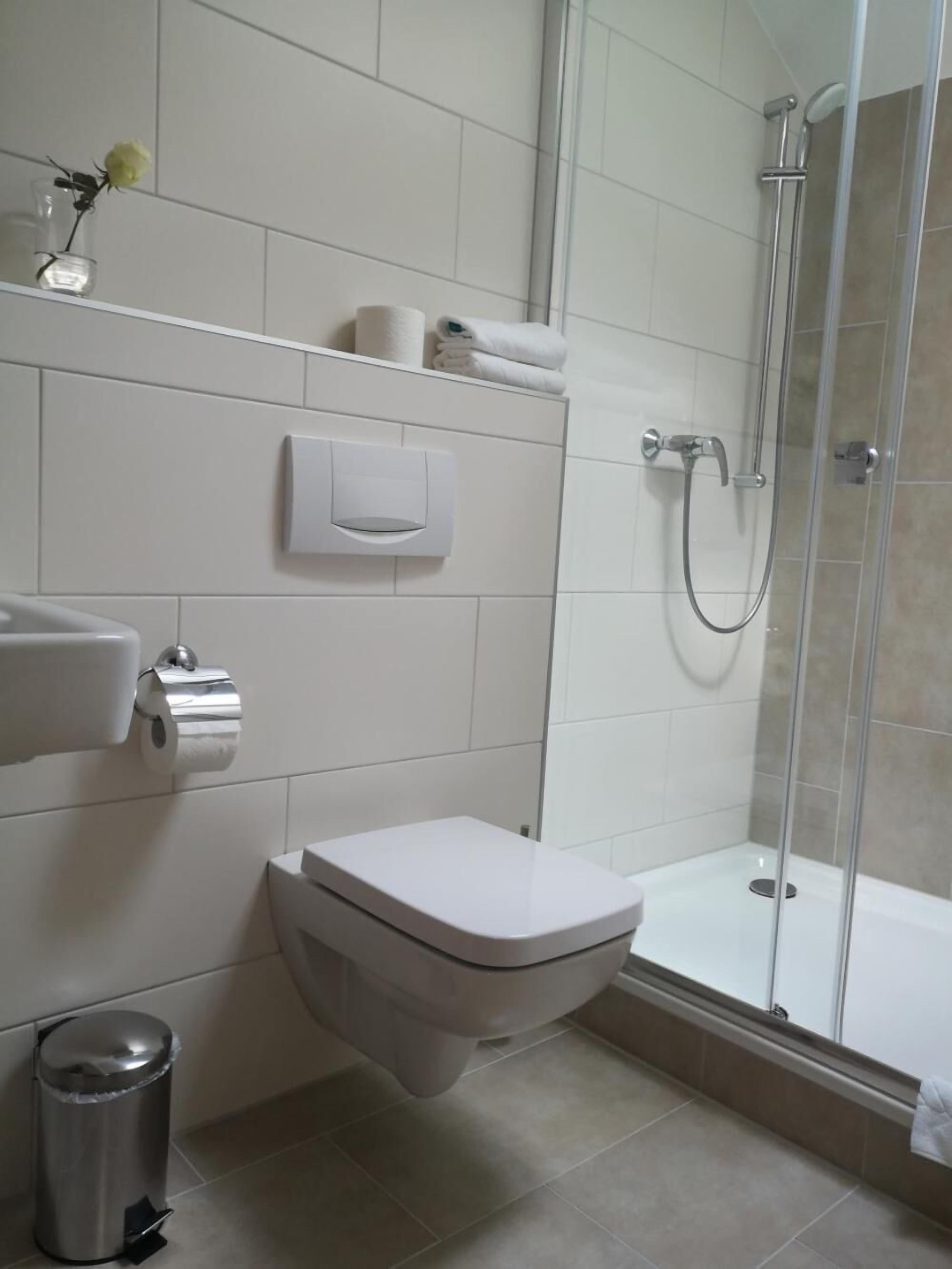 A modern bathroom with a toilet, a hand dryer, a trash bin, and a glass-enclosed shower.