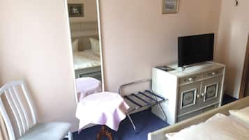A hotel room with a bed, a chair, a small table with a tablecloth, a dresser with a television on top, and a mirror on the wall.