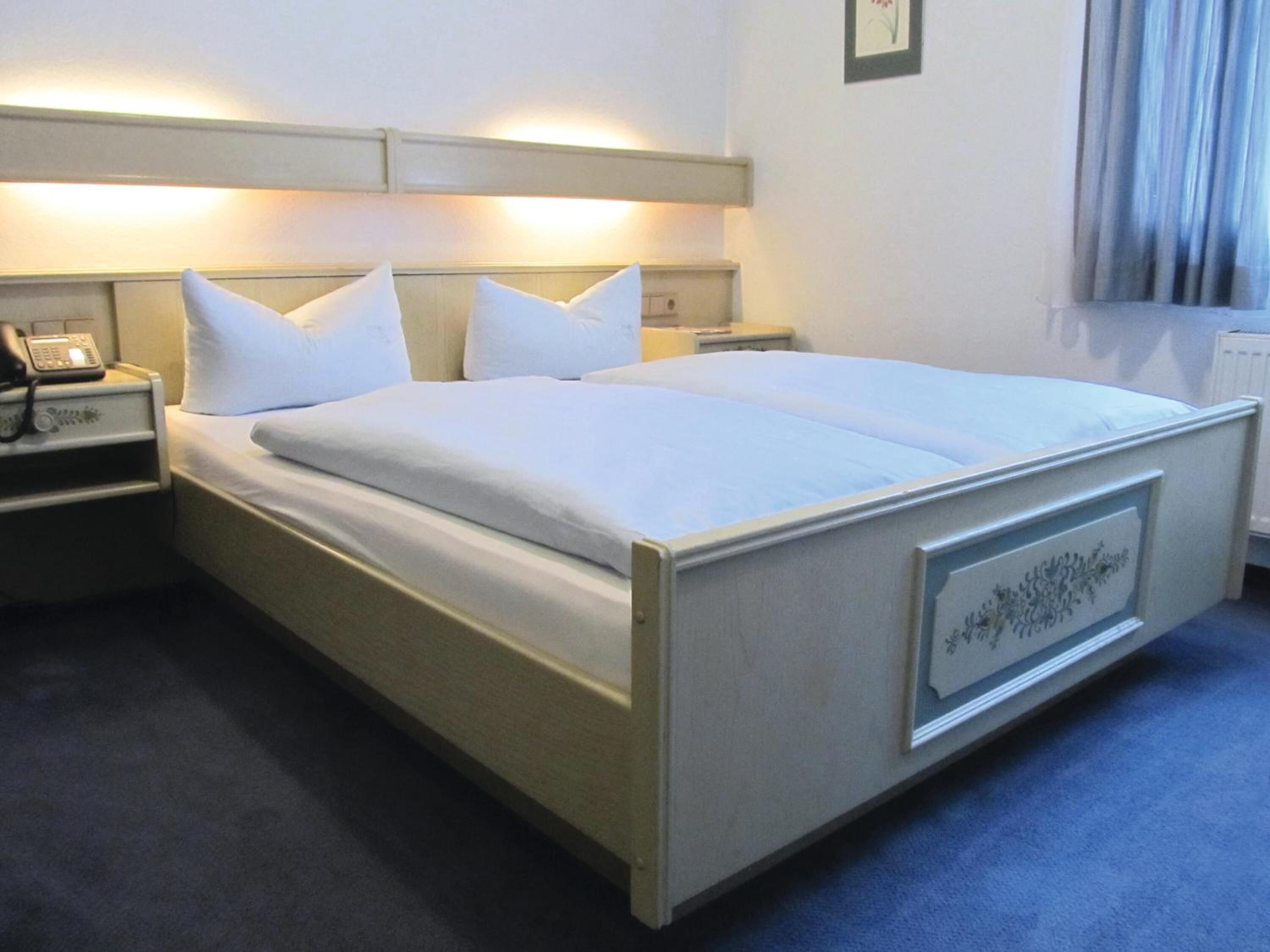 Hotellihuone, jossa on sänky, yöpöydät, puhelin ja patteri.