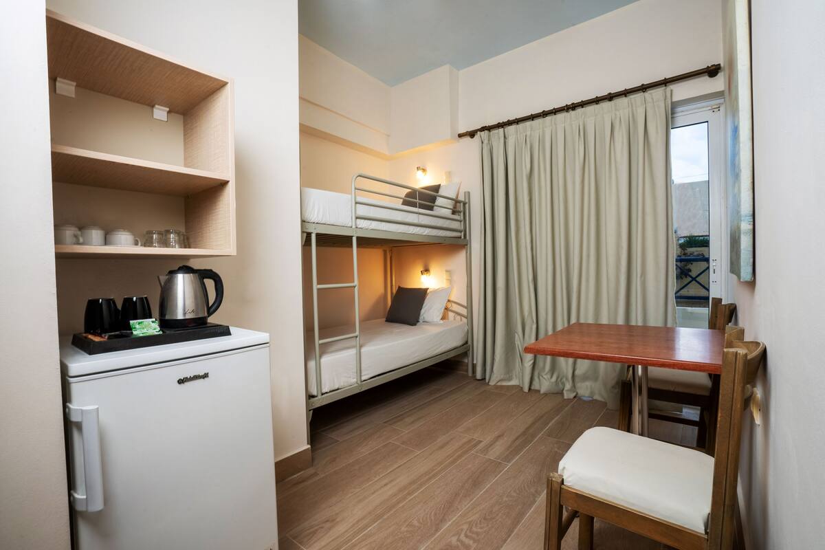 Quarto compacto com beliches, pequena cozinha e área de refeições.