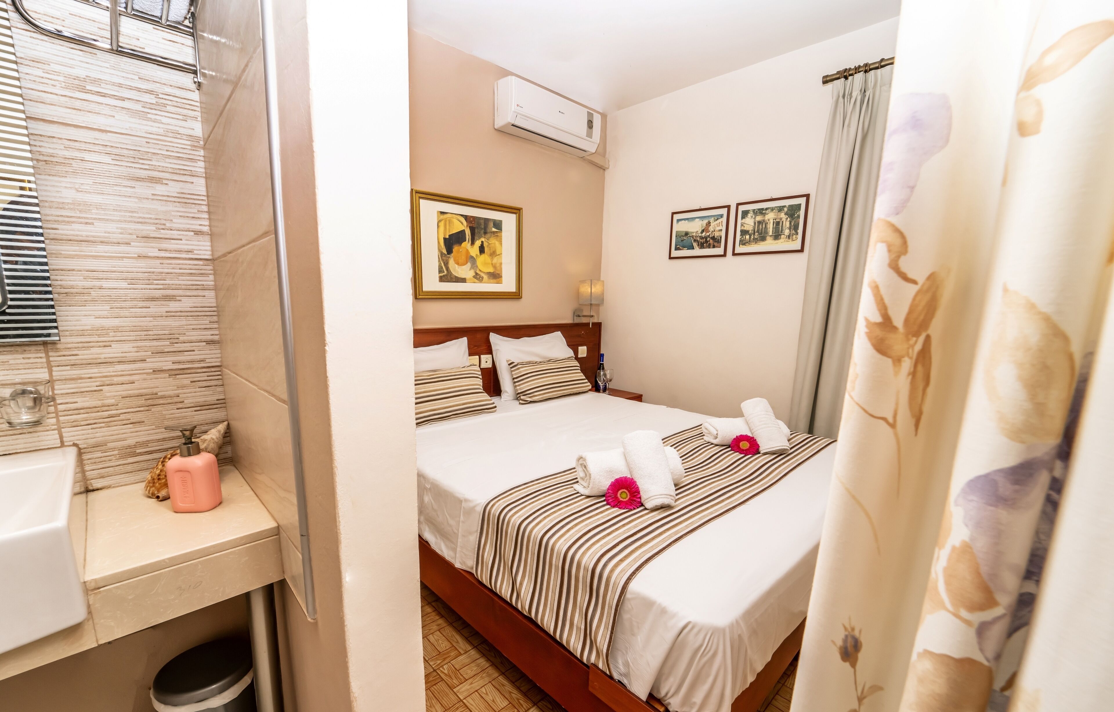 A hotel room with a bed, a bedside table with a bottle, a mirror, and a window with curtains.