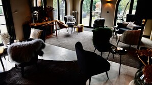 A spacious living area with a high ceiling, large arched windows, and a variety of seating options including a fur-covered chair, a black armchair, and a sofa. - Hostellerie Ten Lande (Beernem)