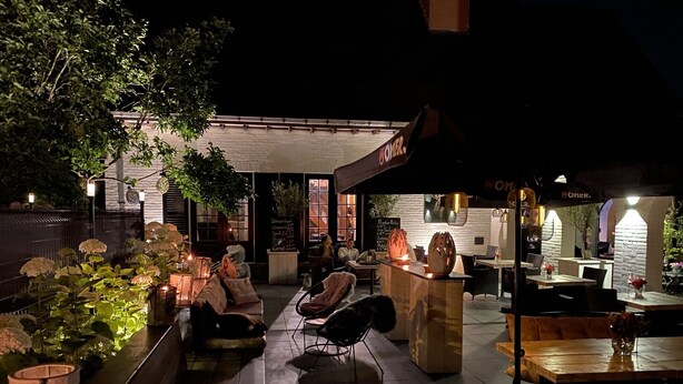 An outdoor seating area with tables and chairs, a bar area, and a building with a sign that reads "BOMER". - Hostellerie Ten Lande (Beernem)