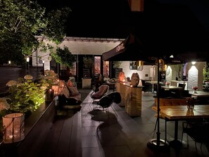 An outdoor seating area with tables and chairs, a bar area, and a building with a sign that reads "BOMER". - Hostellerie Ten Lande (Beernem)