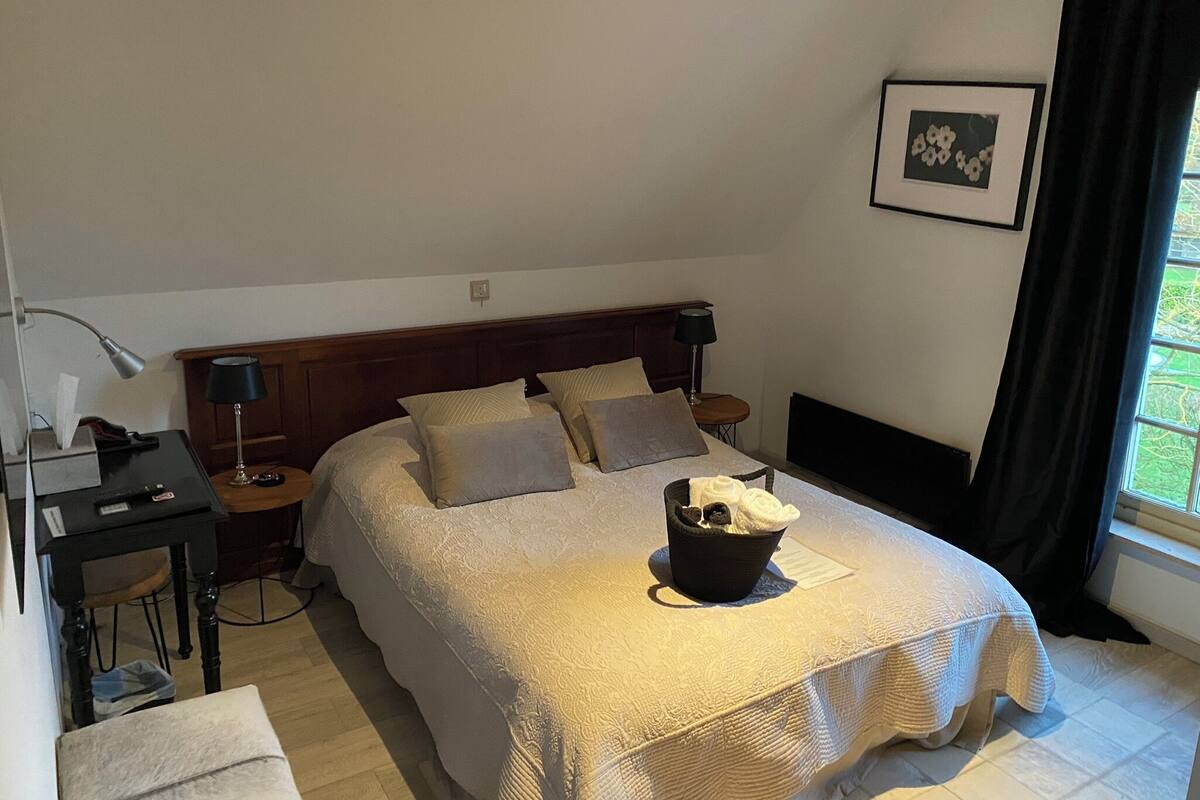 A neatly arranged bedroom with a large bed, bedside tables, a lamp, and a window with curtains.