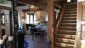 A spacious living area with a wooden staircase, a chandelier, and a dining table set with food. - Hostellerie Ten Lande (Beernem)