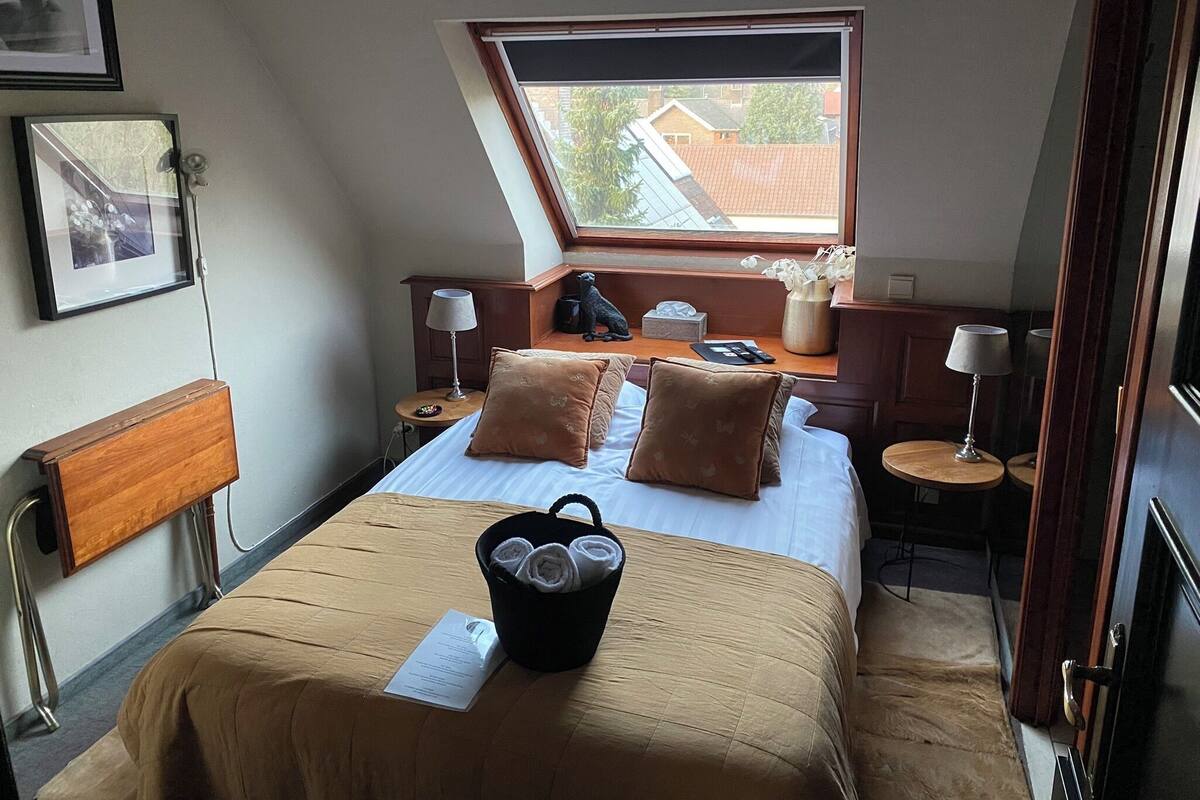 A bedroom with a bed, a window, a nightstand, a lamp, and a small table.