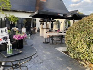 An outdoor seating area with tables and chairs, umbrellas, and a sign indicating social distancing measures. - Hostellerie Ten Lande (Beernem)