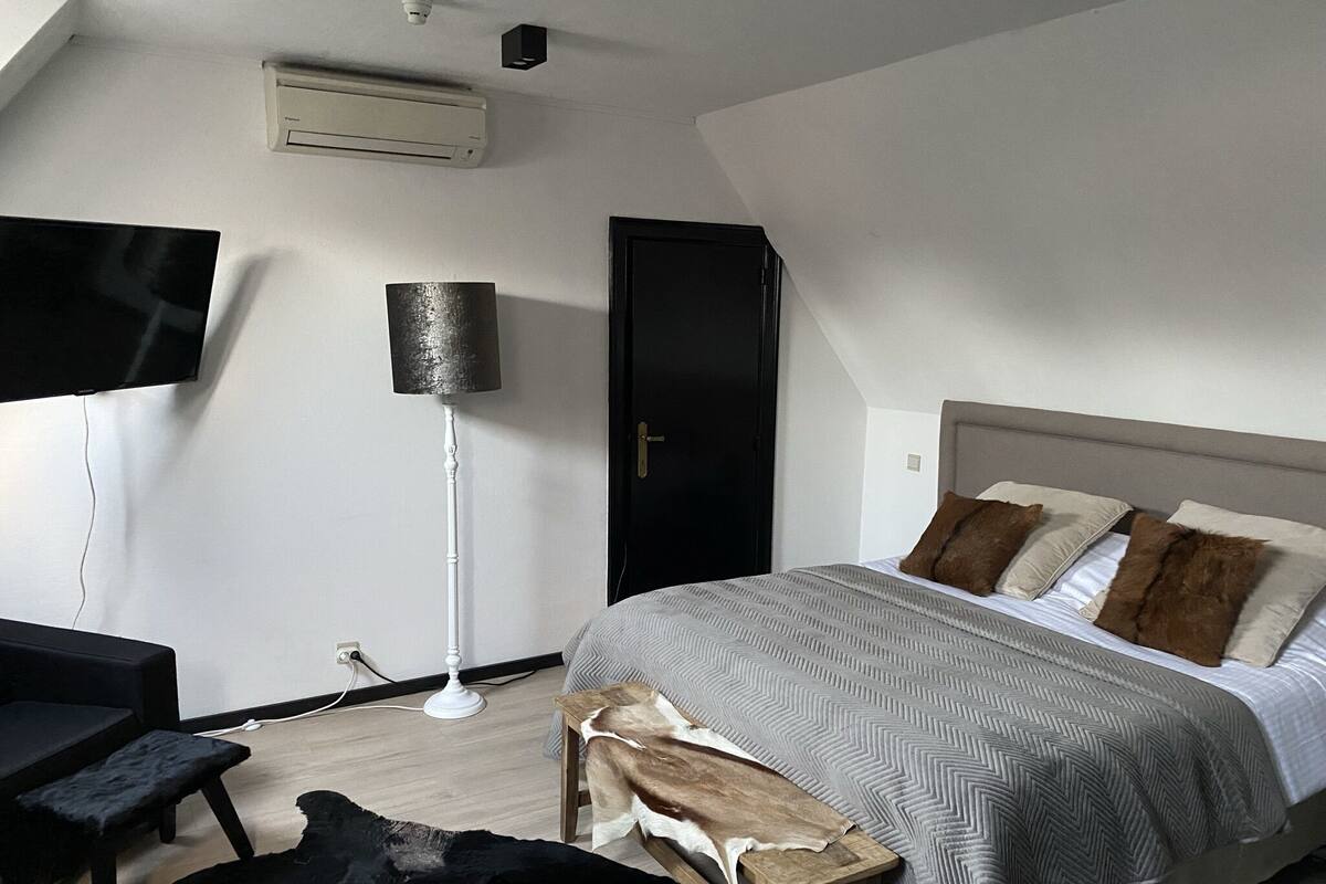 A bedroom with a bed, a desk, a chair, a floor lamp, and a wardrobe.