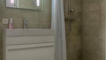 A modern bathroom with a white vanity, a glass-encased mirror, a shower with a white curtain, and a towel rack with red towels.
